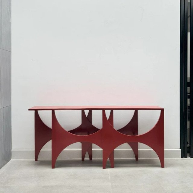 Peer Console handcrafted from solid wood featuring a geometric sculptural pedestal base with semi-circular cut-outs and a matte red finish.